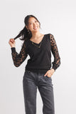 Woman wearing a black long-sleeve top with lace sleeves and gray jeans on a white background